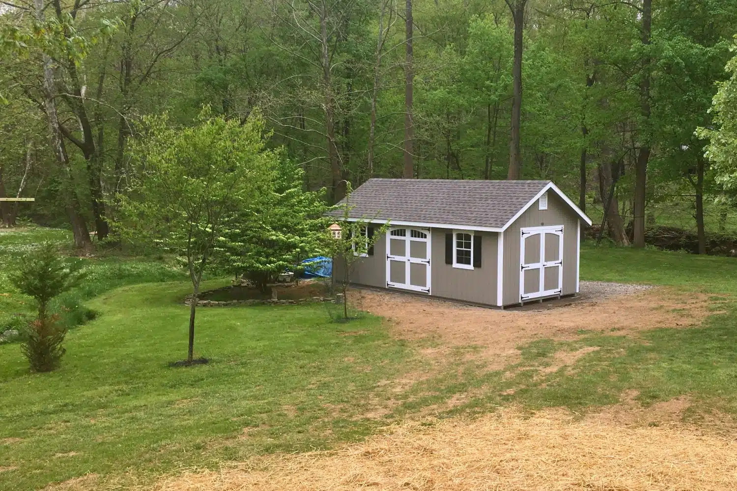 The Designer Workshop Shed 2 Beige and white designer workshop shed of to the distance in patchy lawn in front of trees