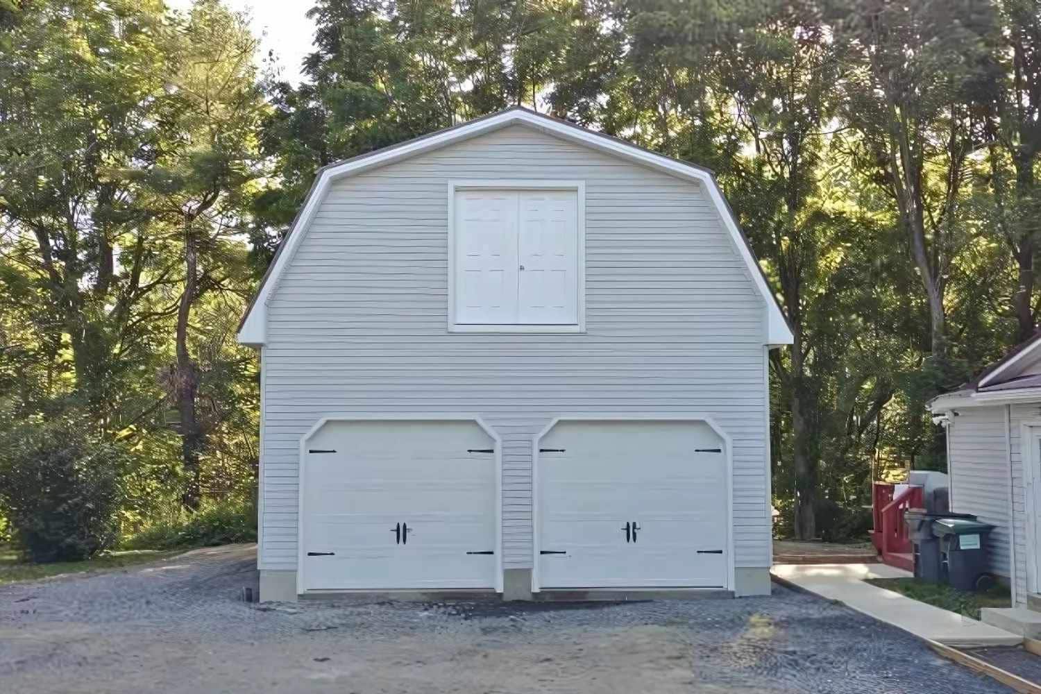 White gambrel garage with two white garage doors and double door on gravel driveway