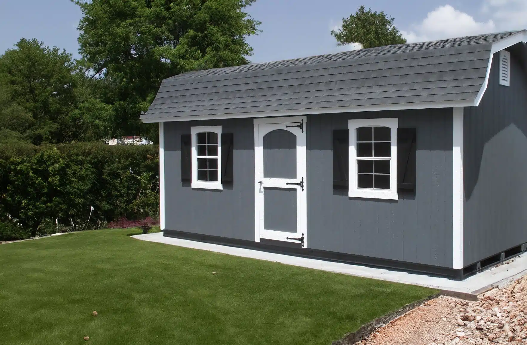 The Designer High Barn Shed 2 Gray and white wood designer high barn shed on concrete pad in backyard grass