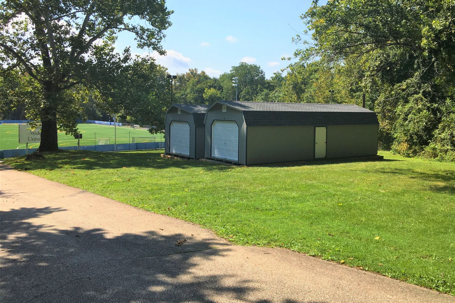 Two standard high barn garage sheds in a grass field in front of a soccer field