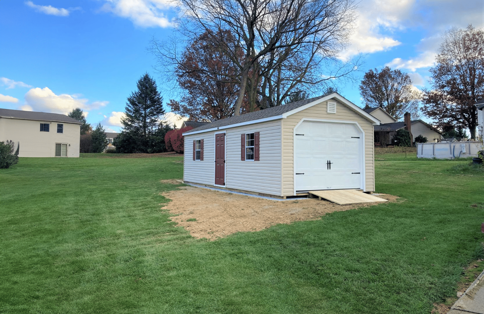 Beige vinyl Standard workshop garage shed with brown door and shutters. Garage door is white vinyl with black handles and wooden ramp